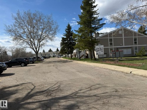 Multi-level building with neutral-toned siding, mature evergreen trees, visible parking areas, and established perimeter landscaping - 5 2204 118 Street, Edmonton, AB - Outdoor