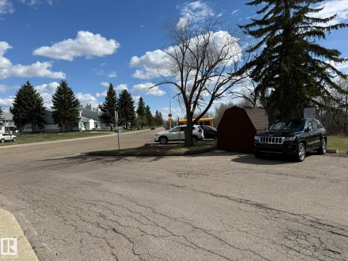 Paved parking area featuring a storage shed with shingled roof, mature trees, and street access - 5 2204 118 Street, Edmonton, AB - Outdoor