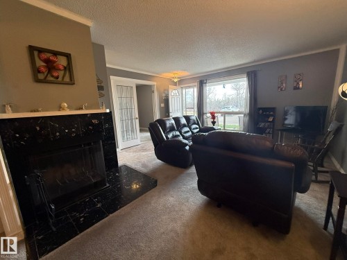 Living area featuring a black tiled fireplace with a white mantel, light gray wall paint, and gray carpeted flooring - 5 2204 118 Street, Edmonton, AB - Indoor Photo Showing Living Room With Fireplace