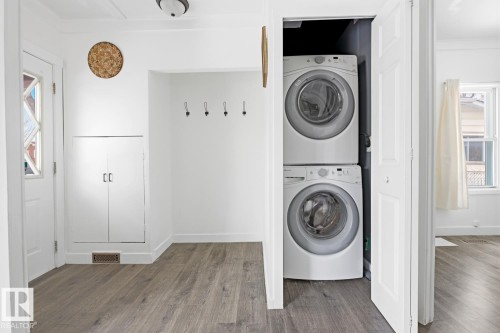 This space features light-colored flooring, white walls, and a stackable washer and dryer unit - 10927 93 Street Nw, Edmonton, AB - Indoor Photo Showing Laundry Room