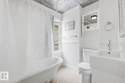 Bathroom featuring a white clawfoot bathtub, a window providing natural light, wainscoting, and a tin ceiling - 