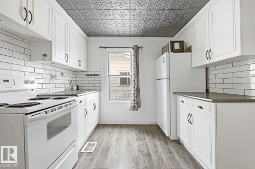 The kitchen features white cabinetry with dark hardware, a white subway tile backsplash, and a tin-style ceiling - 10927 93 Street Nw, Edmonton, AB - Indoor Photo Showing Kitchen