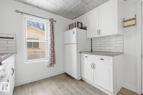 This kitchen features white cabinetry, a subway tile backsplash, and a window with a patterned curtain - 10927 93 Street Nw, Edmonton, AB - Indoor Photo Showing Kitchen