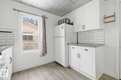 This kitchen features white cabinetry, a subway tile backsplash, and a window with a patterned curtain - 