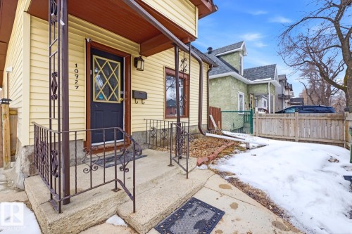 The property features a concrete porch with decorative metal railings, a dark-colored front door with a diamond-patterned window, and light yellow siding - 10927 93 Street Nw, Edmonton, AB - Outdoor