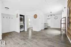 The property features light-colored plank flooring, white walls, and a recessed laundry area with a stacked washer and dryer - 