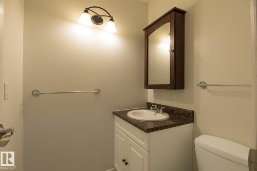 Bathroom featuring a white vanity with a dark speckled countertop, an oval undermount sink, and a chrome faucet - 8039 27 Avenue, Edmonton, AB - Indoor Photo Showing Bathroom
