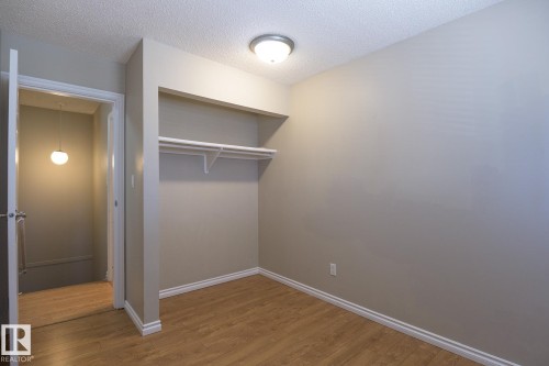 Room featuring wood-finish flooring, light grey painted walls, white trim, and a built-in closet with shelving and a hanging rod - 8039 27 Avenue, Edmonton, AB - Indoor Photo Showing Other Room