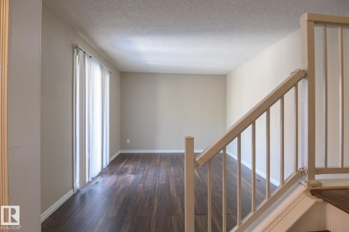 Spacious main living area featuring dark wood-finish flooring, light neutral wall tones, and a sliding glass door with vertical blinds - 8039 27 Avenue, Edmonton, AB - Indoor Photo Showing Other Room