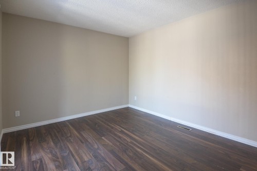 Spacious room featuring rich wood-finish flooring, neutral wall tones, white baseboards, and a textured ceiling - 8039 27 Avenue, Edmonton, AB - Indoor Photo Showing Other Room
