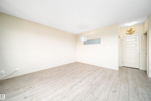 Spacious room featuring light wood-finish flooring, a contemporary chandelier, a white five-panel door, and neutral-toned walls - 421 4008 Savaryn Drive, Edmonton, AB - Indoor Photo Showing Other Room