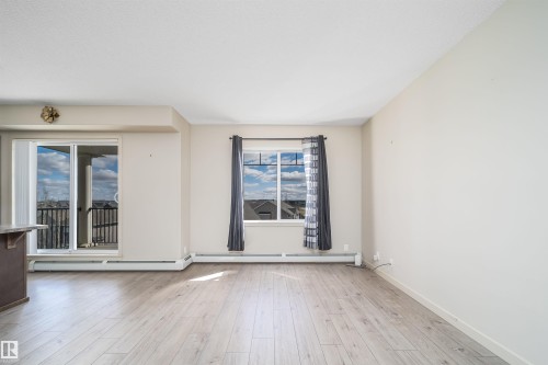 Spacious open-concept room featuring light wood-finish flooring, neutral wall tones, and overhead textured ceilings - 421 4008 Savaryn Drive, Edmonton, AB - Indoor