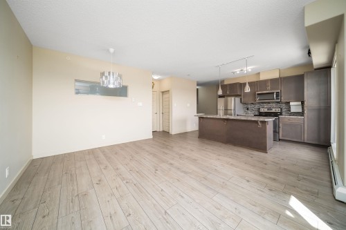 Open-concept living space featuring wood-finish flooring, a contemporary chandelier, and a pass-through window - 421 4008 Savaryn Drive, Edmonton, AB - Indoor Photo Showing Kitchen