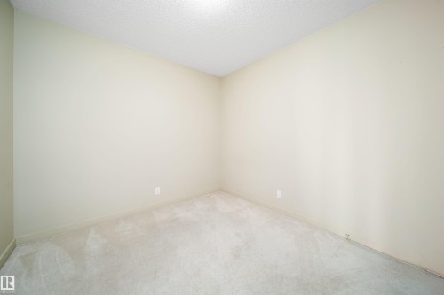 Room featuring neutral-toned walls, textured ceiling, and light-colored carpet flooring - 421 4008 Savaryn Drive, Edmonton, AB - Indoor Photo Showing Other Room