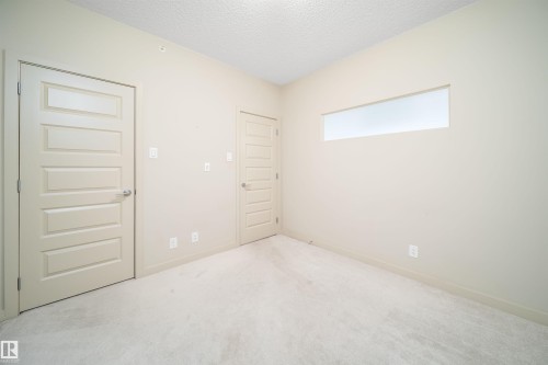 Neutral-toned room featuring a large rectangular transom window, light-colored carpet, and two five-panel interior doors with brushed nickel hardware - 421 4008 Savaryn Drive, Edmonton, AB - Indoor Photo Showing Other Room