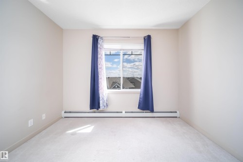 Bedroom featuring a window with white trim, light-colored carpeting, baseboard heating, and neutral painted walls - 421 4008 Savaryn Drive, Edmonton, AB - Indoor Photo Showing Other Room