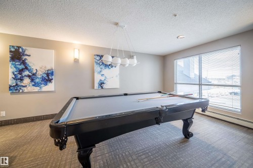 Recreation room featuring a pool table, patterned carpet flooring, and a large window with horizontal blinds - 421 4008 Savaryn Drive, Edmonton, AB - Indoor Photo Showing Other Room