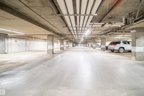 Spacious underground parking facility with concrete flooring, exposed concrete ceilings, and ample overhead lighting - 421 4008 Savaryn Drive, Edmonton, AB - Indoor Photo Showing Garage