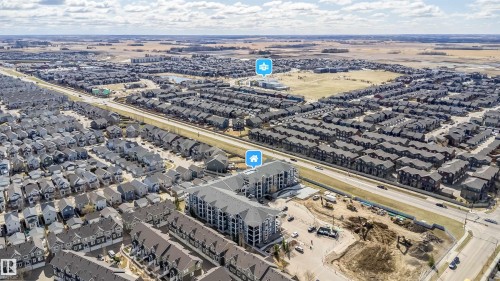 Expansive aerial perspective showcasing a developed residential neighborhood with a multi-story apartment building, single-family homes, and a commercial road - 421 4008 Savaryn Drive, Edmonton, AB - Outdoor With View