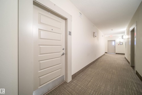 Corridor featuring a textured carpet runner, white paneled doors, and wall-mounted light fixtures - 421 4008 Savaryn Drive, Edmonton, AB - Indoor Photo Showing Other Room