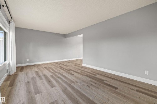 Spacious room featuring wood-finish flooring, light grey walls, and white baseboards - 7927 71 Avenue, Edmonton, AB - Indoor Photo Showing Other Room