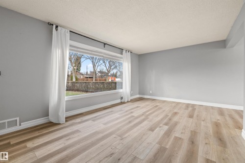 Spacious room featuring a large picture window, light wood-finish flooring, light gray wall paint, and white baseboards - 7927 71 Avenue, Edmonton, AB - Indoor Photo Showing Other Room