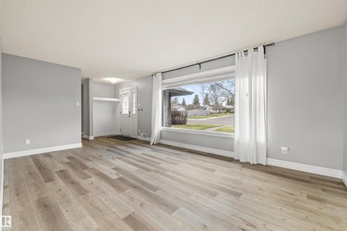 Bright living area featuring wood-finish flooring, a large picture window, and a white paneled entry door with decorative glass inserts - 7927 71 Avenue, Edmonton, AB - Indoor Photo Showing Other Room