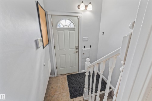 Entryway featuring a white paneled door with an arched window, tiled flooring, and a white painted staircase with a balustrade - 7927 71 Avenue, Edmonton, AB - Indoor Photo Showing Other Room