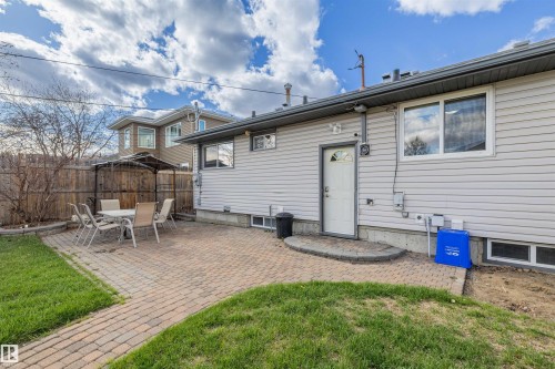 Rear exterior featuring light-colored siding, multiple windows, and a paved patio area - 7927 71 Avenue, Edmonton, AB - Outdoor With Exterior