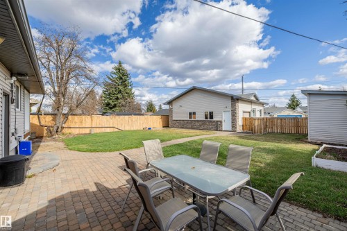 Expansive backyard featuring a paver patio, a large grass area, a wood privacy fence, and a detached structure with a stone veneer and siding exterior - 7927 71 Avenue, Edmonton, AB - Outdoor With Deck Patio Veranda