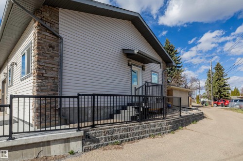 Exterior featuring light grey siding with stone veneer accents, black metal railings, a concrete foundational platform, and a paved side access - 7927 71 Avenue, Edmonton, AB - Outdoor