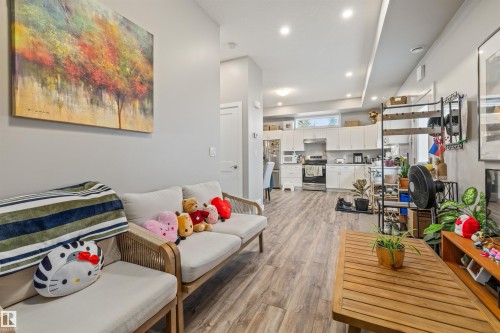 Open-concept living space featuring wood-finish flooring, recessed lighting, and a kitchen with white cabinetry and stainless steel appliances - 7927 71 Avenue, Edmonton, AB - Indoor