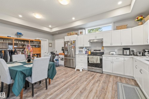 Open-concept kitchen featuring white cabinetry, stainless steel appliances, and a wood-finish flooring - 7927 71 Avenue, Edmonton, AB - Indoor Photo Showing Other Room