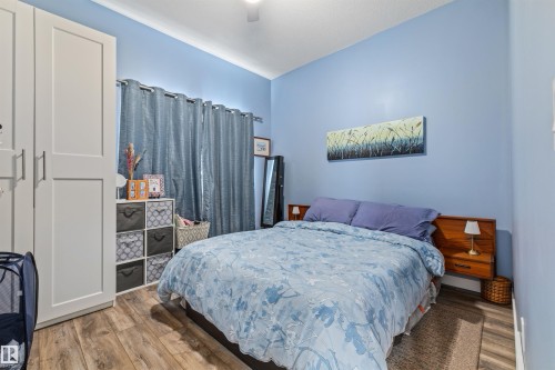Bedroom featuring wood-finish flooring, built-in white wardrobe with shaker-style doors, and light blue walls - 7927 71 Avenue, Edmonton, AB - Indoor Photo Showing Bedroom