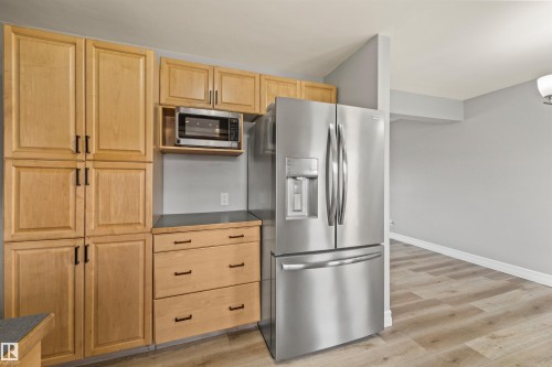 Stainless steel French door refrigerator, wood-finish flooring, light wood cabinetry, integrated microwave, and dark countertop - 7927 71 Avenue, Edmonton, AB - Indoor Photo Showing Kitchen