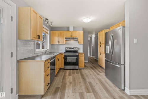 Kitchen featuring light wood cabinetry, stainless steel appliances, dark countertops, a white subway tile backsplash, and wood-finish flooring - 7927 71 Avenue, Edmonton, AB - Indoor Photo Showing Kitchen With Double Sink