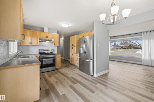Kitchen featuring wood-finish flooring, light wood cabinetry, stainless steel appliances, and a tile backsplash - 7927 71 Avenue, Edmonton, AB - Indoor Photo Showing Kitchen