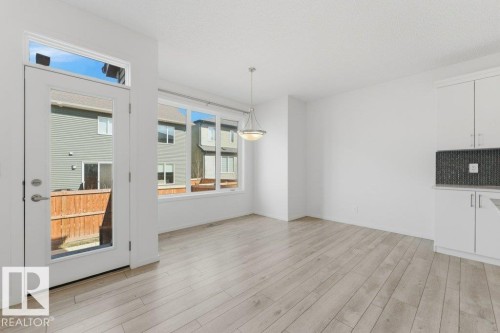 Open-concept area featuring light wood-finish flooring, a full-light exterior door with transom window, and a wall of windows - 2011 207 Street, Edmonton, AB - Indoor