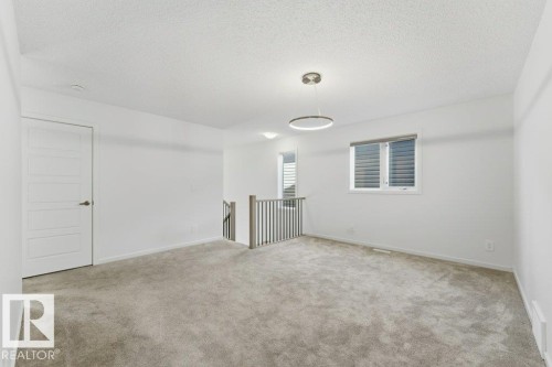 Carpeted bonus room featuring a contemporary circular pendant light, a window with horizontal blinds, a white paneled door, and a staircase with a dark metal railing - 2011 207 Street, Edmonton, AB - Indoor Photo Showing Other Room