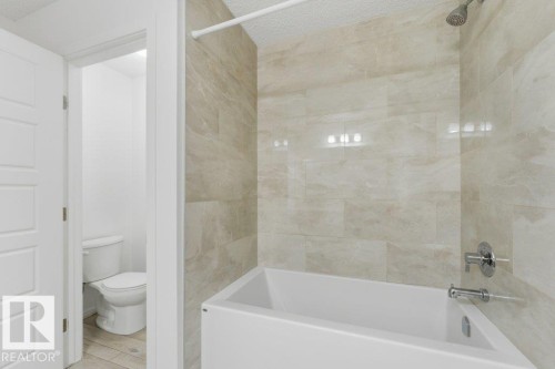 White porcelain bathtub with chrome fixtures and light-toned, large format wall tiling - 2011 207 Street, Edmonton, AB - Indoor Photo Showing Bathroom