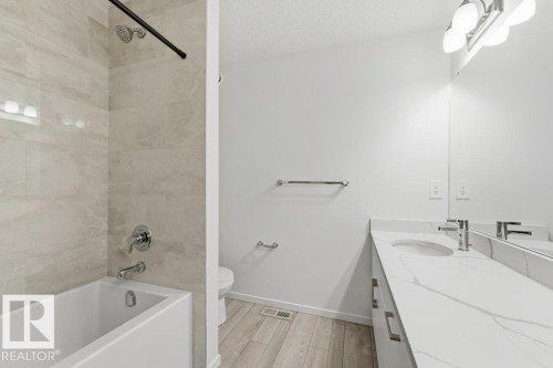Modern bathroom featuring a white bathtub with chrome fixtures, large format tiled shower surround, a vanity with a white countertop and integrated sink, chrome faucet, and wood-finish flooring - 2011 207 Street, Edmonton, AB - Indoor Photo Showing Bathroom