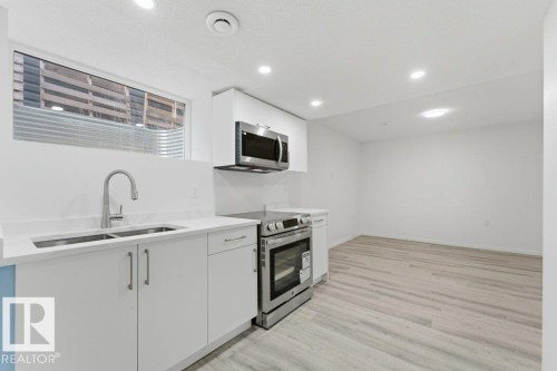 Contemporary kitchen area featuring wood-finish flooring, white cabinetry, a stainless steel double sink with a gooseneck faucet, white countertops, and recessed ceiling lighting - 2011 207 Street, Edmonton, AB - Indoor Photo Showing Kitchen With Double Sink With Upgraded Kitchen