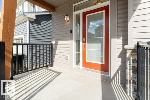 Inviting front porch featuring a vibrant red entry door with glass panels, light-colored siding, dark metal railings, and a stone-clad pillar - 2011 207 Street, Edmonton, AB - Outdoor With Exterior