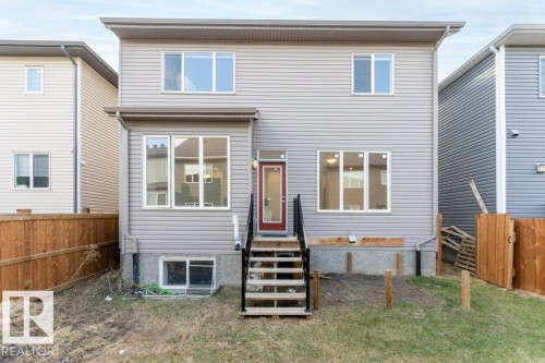 Rear exterior elevation featuring light gray horizontal siding, a red paneled entry door, a two-story design, multiple white-framed windows, and a partially grassed rear yard - 2011 207 Street, Edmonton, AB - Outdoor