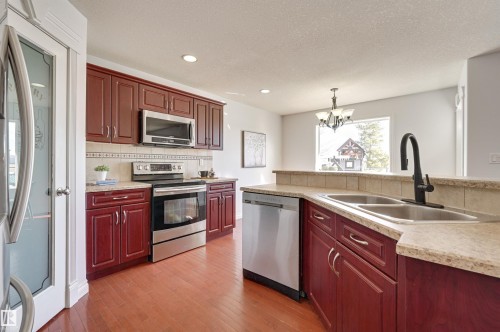 The kitchen features rich wood cabinetry, stainless steel appliances, a double basin sink with a modern faucet, and light-toned countertops - 24 Birchmont Drive, Leduc, AB - Indoor Photo Showing Kitchen With Stainless Steel Kitchen With Double Sink