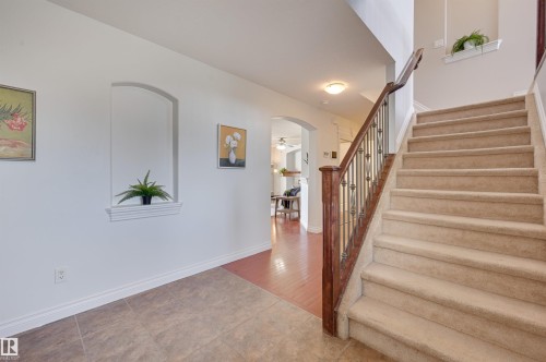 Entryway featuring a carpeted staircase with a dark wood handrail and wrought iron balusters, tile flooring, and an arched wall niche - 24 Birchmont Drive, Leduc, AB - Indoor Photo Showing Other Room