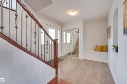 The entryway features tiled flooring, a built-in bench, and a staircase with a wooden handrail and wrought iron balusters - 