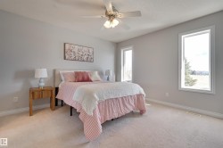 The room features light-colored walls and carpeting, a ceiling fan with integrated lighting, and two windows providing natural light - 