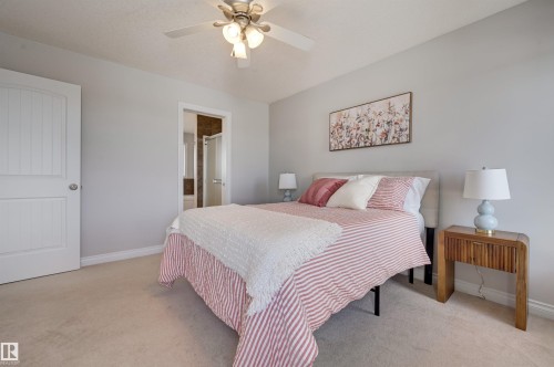 This sleeping area features light-colored carpeting and walls, a ceiling fan with integrated lighting, and a white paneled door - 24 Birchmont Drive, Leduc, AB - Indoor Photo Showing Bedroom