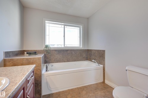 Bathroom featuring a white bathtub, a window with decorative muntins, and tiled flooring and walls - 24 Birchmont Drive, Leduc, AB - Indoor Photo Showing Bathroom